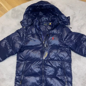 Polo Ralph Lauren dunjacka - Snygg blå dunjacka från Polo Ralph Lauren. Köptes på sommaren för 4999kr. Den är oanvänd då jag har en annan jacka. Kommer passa dig bra ifall du vill ha en fet stil. Kan fraktas och hämtas upp. Priset är inte hugget i sten. Säljer den då jag behöver pengar