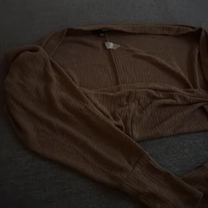 Beige bolerotopp - Säljer en stilren beige bolerotopp med långa ärmar. Perfekt för att lägga till en extra touch till din outfit. Toppen har en mjuk och bekväm känsla.