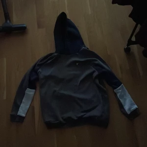 Mörkblå hoodie med vita detaljer från Lyle&Scott  - Säljer en mörkblå hoodie från Lyle & Scott med vita detaljer på ärmarna. Den har en broderad logotyp på bröstet och en klassisk huva. Perfekt för en avslappnad stil. KÖPT FÖR 599kr.  SÄLJS FÖR 399kr. SKICK 7-8 av 10. Tveka inte på att höra av er. STORLEK 15-16 år