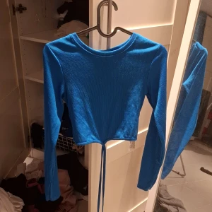 Blå ribbad topp från Amisu - Säljer en snygg blå ribbad topp från Amisu. Den är croppad med långa ärmar och har en knytning framtill. Perfekt för en trendig look!