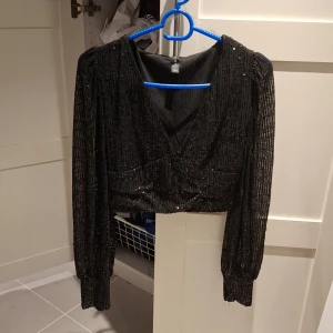 Svart glittrig croppad topp - Säljer en svart glittrig croppad topp från new yorker med långa ärmar och v-ringning.