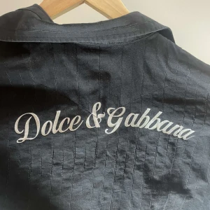 Svart kortärmad skjorta från Dolce & Gabbana - Snygg svart skjorta från Dolce & Gabbana med korta ärmar och stilren design. Skjortan har en broderad logga på bröstet och en klassisk krage. Perfekt för en trendig look. Skjortan är liten i storleken mer som en storlek S.