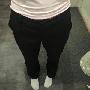 Svarta kostymbyxor - Snygga svarta kostymbyxor med en klassisk design. De har en normal passform och är perfekta för en stilren look. Byxorna har en dragkedja och knappar framtill.