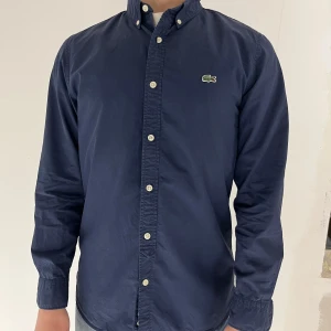Lacoste Live skjorta - Fin skjorta från Lacoste Live i marinblå färg. Den är i storleken small. Modellen är 173cm och väger 65kg. 