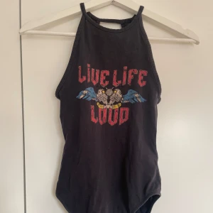 Svart bodysuit med tryck - Cool svart bodysuit med texten 'Live Life Loud' och ett tryck av en motorcykel med vingar. Den har en hög hals och är ärmlös, perfekt för en edgy look.