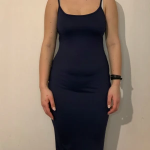 Mörkblå tight klänning - Snygg mörkblå klänning med smala axelband och en tight passform. Perfekt för en stilren look. Klänningen är ärmlös och har en enkel design som framhäver figuren.