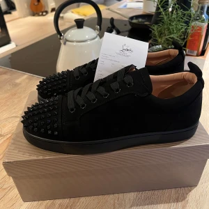 Svarta sneakers med nitar från Christian Louboutin - Snygga svarta sneakers från Christian Louboutin med nitar på tån och den ikoniska röda sulan. Skorna har snörning och är tillverkade i mocka för en lyxig känsla. Perfekta för att ge din outfit en edgy touch. Priset är inte hugget i sten så kom gärna med rimliga bud, skriv gärna vid frågor eller funderingar.