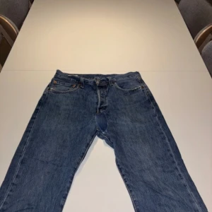 Levis 501 jeans i blå denim - Säljer ett par klassiska Levis 501 jeans i blå denim. Dessa jeans har en rak passform och är tillverkade av högkvalitativt denimtyg. Perfekta för en avslappnad stil.