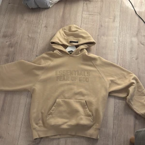 Beige hoodie från Essentials Fear of God - Säljer en äkta beige hoodie från Essentials Fear of God. Den har en stor ficka framtill och en bekväm huva. Perfekt för en avslappnad stil. Har digitalt kvitto kan skickas om man ber om det storlek S passar M ny pris 2000kr 