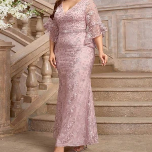 Rosa långklänning med spets och pärlor - Elegant rosa långklänning med v-ringning och vackra spetsdetaljer. Klänningen har trekvartsärmar med volang och är dekorerad med pärlor och broderier. Perfekt för festliga tillfällen. Har två olika storlek en av de är 1XL och den andra är 2XL..