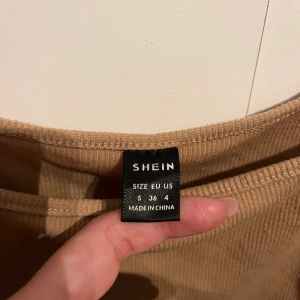 Beige ribbad klänning från Shein - Snygg beige klänning från Shein i ribbat material. Klänningen har en åtsittande passform och är ärmlös med knytbara detaljer på sidorna. Perfekt för en stilren look. Framhäver kurvorna snyggt!