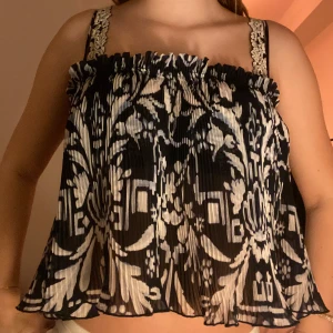 Svart och vit mönstrad topp - Snygg svart och vit topp med ett unikt mönster. Den har smala axelband och en luftig passform, perfekt för varma dagar. Toppen är plisserad vilket ger en fin struktur och rörelse.