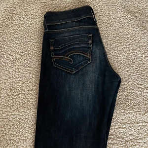 Lågmidjade Mörkblå jeans från Mavi - Snygga low waist mörkblå jeans från Mavi med klassisk femficksdesign och dekorativa sömmar på bakfickorna. .