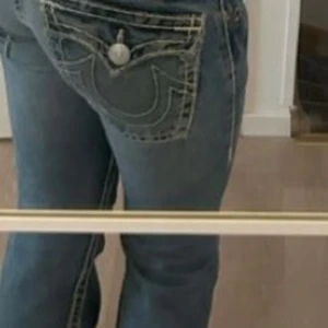  jeans från True Religion(SÖKER BYTE) - Snygga blå jeans från True Religion med distinkta vita sömmar och en knappdetalj på bakfickan. Perfekta för en avslappnad stil med en touch av attityd.