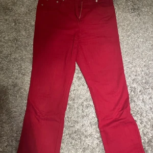 Röda jeans byxor med broderad ficka - Snygga röda byxor med en unik broderad detalj på bakfickan. Byxorna har en dragkedja framtill och är perfekta för att ge en färgklick till din outfit.