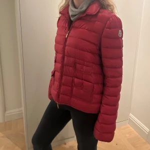 Vinröd dunjacka från Moncler - Snygg vinröd dunjacka från Moncler med dragkedja och två fickor framtill. Jackan har en quiltad design och långa ärmar, perfekt för kyligare dagar. Den har en klassisk passform och Moncler-logga på ärmen. Köpt för ett tag sedan på nk. Mycket unik och fin färg till vår och höst. Storlek 3 vilket motsvarar ungefär S/M🥰🥰pris kan diskuteras vid snabbköp och ÄR ÖPPEN FÖR BYTEN