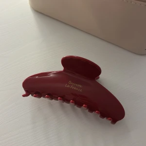 Röd hårklämma  - Elegant röd hårklämma från Barrette La France. Perfekt för att hålla håret på plats med stil. Klämman har en glansig yta och en klassisk design som passar till alla tillfällen. Köpt på en marknad utomlands! Använd en gång!