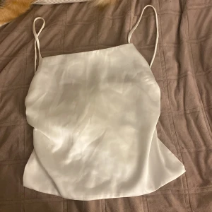 Vit sidenlinne från Zara - Säljer ett vitt sidenlinne från Zara med tunna axelband med knyten i ryggen. Den har aldrig blivit andvänd. Skriv fär mer bilder. 
