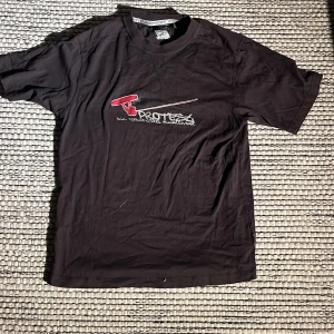 Svart t-shirt från Protest - Säljer en svart t-shirt från Protest med tryck på framsidan. Perfekt för en avslappnad stil. Storlek L.