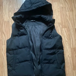 Svart dunväst från Shein - Snygg svart dunväst från Shein med huva och dragkedja. Perfekt för kyligare dagar och enkel att matcha med olika outfits.