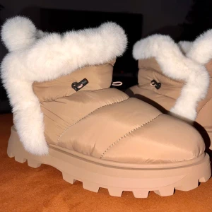 Beige vinterboots med vit päls - Snygga och varma beige vinterboots med vit pälsdetalj runt kanten. De har en robust sula för bra grepp och en praktisk snörning för justerbar passform. Perfekta för kalla vinterdagar.