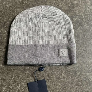 Grå och svart mössa - Snygg och stilren mössa i grått och svart med klassiskt rutigt mönster. Mössan har en uppvikt kant med en broderad. Perfekt för att hålla värmen med stil.