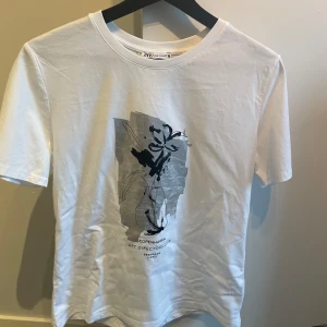 Vit t-shirt med tryck från Zara - Snygg vit t-shirt från Zara med ett konstnärligt tryck i grått och svart på framsidan. Perfekt för en stilren och modern look.
