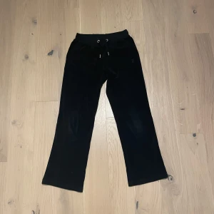 Svarta Juicy Couture byxor - Snygga svarta byxor från Juicy Couture i mjukt material. Byxorna har en bekväm passform med dragsko i midjan och stilrena fickor med knappar baktill. Perfekta för en avslappnad look. De är inte så använda och i bra skick 