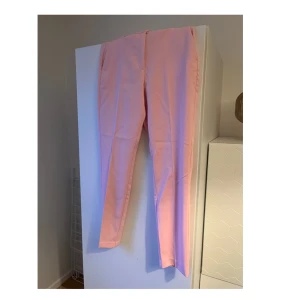 Rosa byxor - Snygga rosa kostymbyxor med en stilren design. De har en rak passform och är perfekta för en färgglad look. Byxorna har hällor för bälte och en klassisk midja.