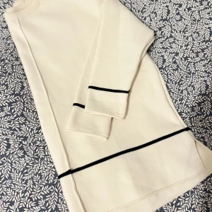 Beige tröja med svarta detaljer - Beige tröja med svarta ränder vid ärmslut och nederkant. Aldrig använd så tröjan är i bra skick. Det är en OneSize tröja, skulle säga att den sitter som en tröja i L.