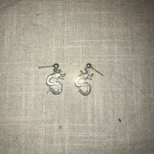 Silvriga drakörhängen - Snygga silvriga örhängen i form av drakar. Perfekta för att ge en unik touch till din stil. De är små och lätta, vilket gör dem bekväma att bära hela dagen.