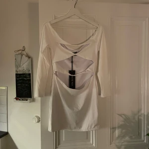 Vit klänning med cut-out detaljer - Trendig vit klänning med unika cut-out detaljer framtill. Klänningen har långärmade och en tight passform, perfekt för en stilren look. Den är gjord i ett mjukt material som ger en bekväm känsla. Storlek L men mer som M. Oanvänd, prislapp kvar.