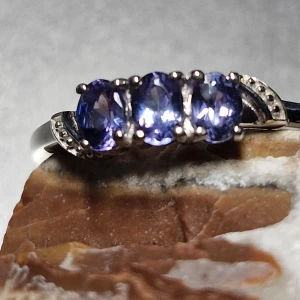 Ring med blå stenar - Elegant ring med tre blå stenar i en rad. Stenarna är ovala och ger en vacker glans. Perfekt för att ge en touch av färg och elegans till din stil.                                              Platinpläterad silver ring med 3 tanzanit stenar  Produkt beskrivning: 925 silver platinpläterad, 1.440  Stenar: 3 ovala tanzaniter ca 4x3 mm, 0.516 ct Ring storleken är 17.0 mm (N)