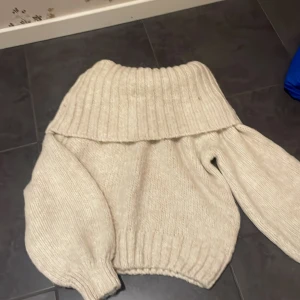 Beige stickad offshoulder tröja - Mysig beige stickad tröja med offshoulder-design och ribbade detaljer. Perfekt för kyliga dagar med sin avslappnade passform och långa ärmar.