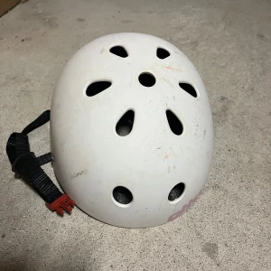 Vit hjälm med ventilationshål - Säljer en vit hjälm med flera ventilationshål och justerbart svart spänne. Perfekt för cykling eller skateboard. Märket syns på sidan av hjälmen.