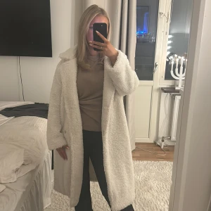 Vit teddyjacka från Bik Bok - Mysig vit teddyjacka från Bik Bok i storlek XS. Jackan har en lång och fluffig design med knappar framtill. Perfekt för kyliga dagar när du vill hålla dig varm och stilren. Inga defekter