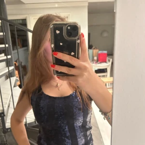 Svart och blå glittrig linne - Snygg svart och blå glittrig linne med smala axelband. Perfekt för en kväll ute eller fest. Den har en åtsittande passform som framhäver figuren.