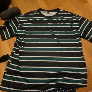 Randig t-shirt - Snygg randig t-shirt i svart, vit och grön. Perfekt för en avslappnad stil. Kortärmad med normal passform.