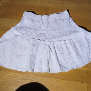 Vit kjol från Bershka - Säljer en söt vit kjol från Bershka med elastisk midja och volangdetaljer. Perfekt för varma sommar. Kjolen går även perfect att använda som en fin sommar topp. Pris går att diskutera som vanligt.