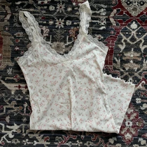 Blommig klänning med spetsdetaljer! - Söt klänning med blommigt mönster i rosa och grönt. Klänningen har spetsdetaljer vid axelbanden och en v-ringad halslinje. I perfekt skick då den endast använts ett fåtal gånger. Inga lappar men den är i storlek xs!  Perfekt för varma sommardagar.