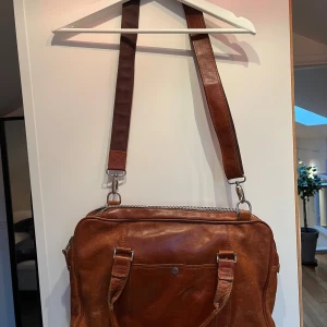 Brun skinnväska från Royal Republic - Snygg brun skinnväska från Royal Republic med justerbar axelrem och dragkedja. Perfekt för att bära dina dagliga nödvändigheter med stil. Väskan har en elegant design och är tillverkad i högkvalitativt skinn.