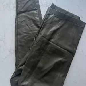 Gröna leggings i syntetmaterial - Snygga gröna leggings i syntetmaterial med en tight passform, hög midja. Perfekta för en stilren look och kan enkelt matchas med olika toppar.