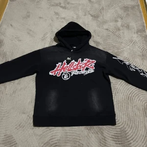  Hellstar Records tour hoodie  - En exklusiv Hellstar Records tour hoodie med tryck fram och bak. Framsidan har ett rött och vitt grafiskt tryck, medan baksidan listar turnédatum och platser. Hoodien har en klassisk passform med långa ärmar och en justerbar huva.