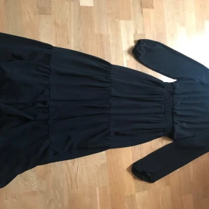 Svart långklänning från Sisters Point - Elegant svart långklänning från Sisters Point med långa ärmar och en smickrande passform. Perfekt för höst- och vinterevenemang. Klänningen har en diskret dragkedja i ryggen för enkel påklädning.