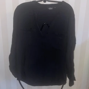 Svart långärmad skjorta från KappAhl - Säljer en stilren svart långärmad skjorta från KappAhl. Skjortan har en v-ringad design och är perfekt för en avslappnad look. Passar bra till både jeans och kjol.