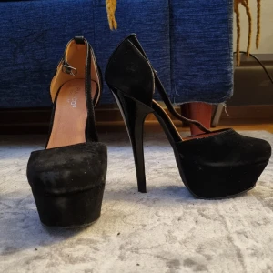 Svarta högklackade pumps - Snygga svarta pumps i strl 36 med hög klack (14cm) och platåsula (4cm). Skorna har en elegant design med en smal rem runt ankeln och en spetsig, men rundad, tå. Perfekta för en kväll ute eller en speciell tillställning. Pga sättet jag går på är insidan av skorna lite nött (se bild 4).