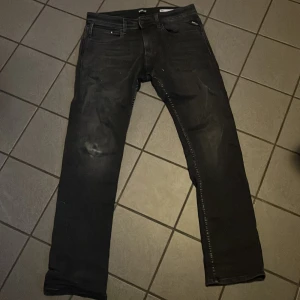Svarta jeans från Replay - Säljer ett par svarta jeans från Replay i modellen Dave med comfort fit. De har en klassisk design med fem fickor och knappgylf. Perfekta för en avslappnad stil. Slitning på höger knä (ej hål) 