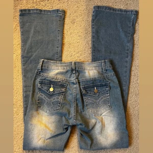 Blå low waist boot cut jeans - Säljer ett par blå jeans med snygga broderade detaljer på bakfickorna. Använt ett fåtal gånger. Har sytt dem lite så dom är lite mer lågmidjade