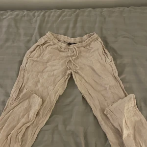 Beige linnebyxor med snörning - Snygga, låg midjade och bekväma beige linnebyxor med elastisk midja och snörning. Perfekta för en avslappnad stil. Passar bra till en enkel topp för en somrig look.