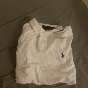 Vit pikétröja från Ralph Lauren - säljer en klassisk vit pikétröja från Ralph Lauren i storlek M. Tröjan har en broderad logotyp i mörkblått på bröstet och är tillverkad i bomull. Perfekt för en stilren och avslappnad look. Köpt för 1300kr